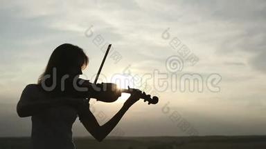 剪影女孩<strong>小提琴</strong>手在日落的天空背景下拉<strong>小提琴</strong>。